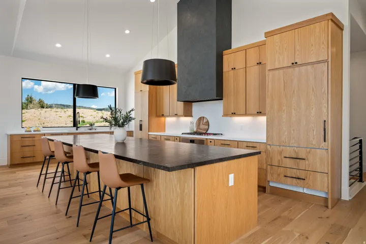 Gourmet kitchen featuring a large central island with a dark countertop, extensive custom wood cabinetry, stainless steel appliances, and a modern range hood