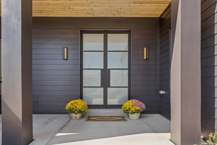 Contemporary entry featuring double glass doors with dark framing, horizontal siding, and a wood-finish ceiling