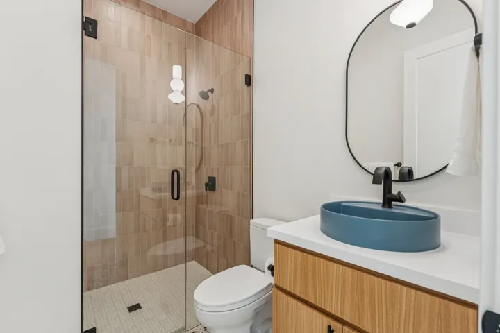 Modern bathroom featuring a frameless glass shower enclosure with wood-finish tile surround and a textured shower pan