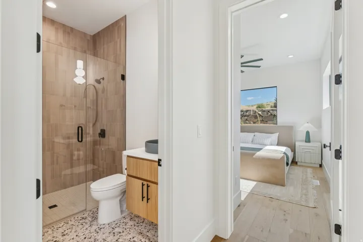 Full bathroom featuring a glass-enclosed shower with vertical tile, a light wood-finish vanity with a dark basin sink, and terrazzo-style flooring