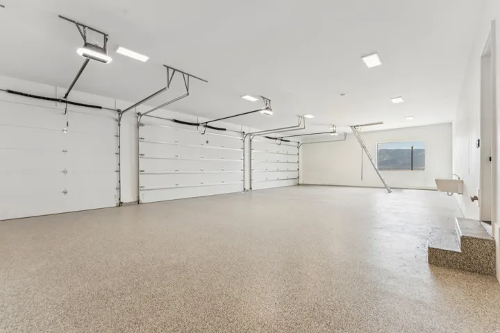 Spacious garage featuring two overhead doors, epoxy-coated flooring, recessed lighting, and a utility sink