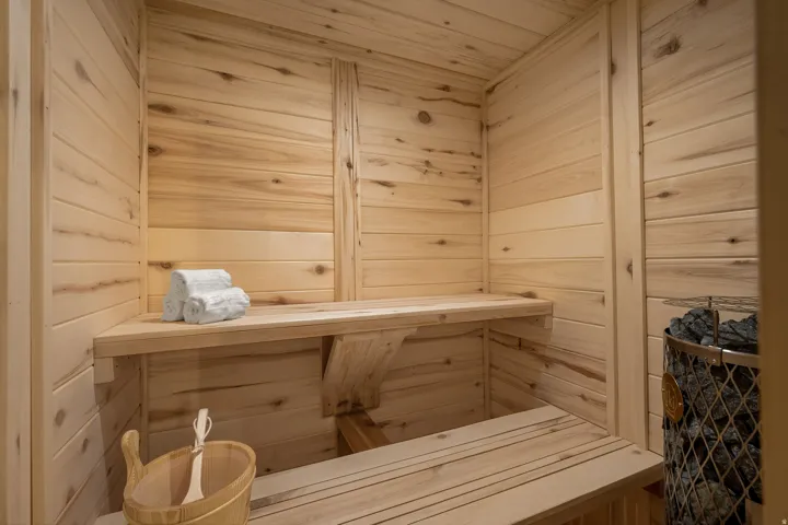 Custom sauna featuring natural wood paneling, multi-level wooden benches, and a built-in stone heater