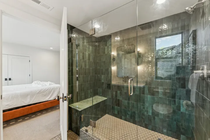 Glass-enclosed shower featuring dark green rectangular tile, hexagonal mosaic floor tile, and a built-in bench