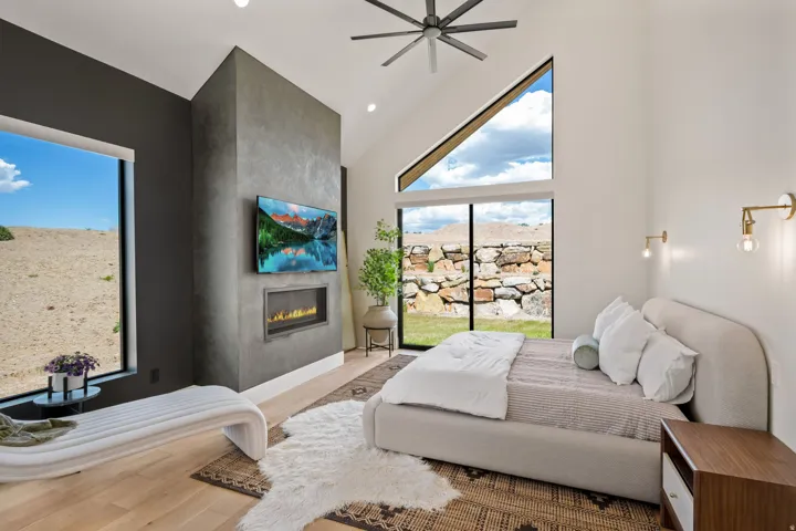 Vaulted ceiling room featuring a sleek fireplace with a television mounting, multiple large windows, a built-in stone wall, and light wood-finish flooring