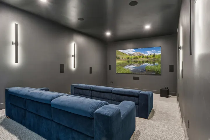 Dedicated media room featuring a large wall-mounted screen, recessed ceiling lighting, and integrated wall speakers