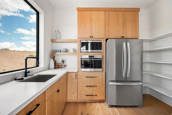 Contemporary kitchen featuring light wood cabinetry, a large picture window, a stainless steel refrigerator, built-in microwave and oven, and a corner pantry with open shelving