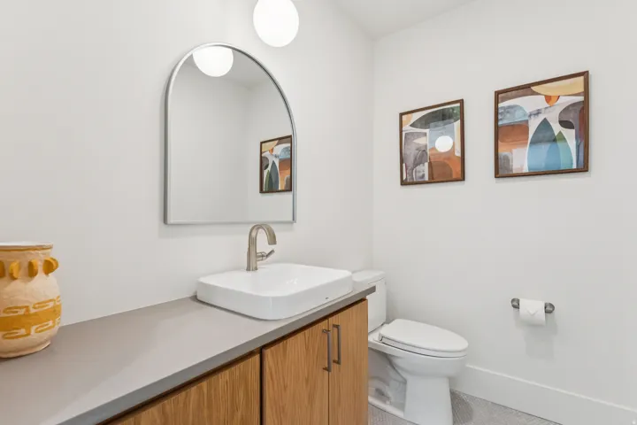 Modern vanity featuring wood-finish cabinetry, a vessel sink, and a sleek arched mirror