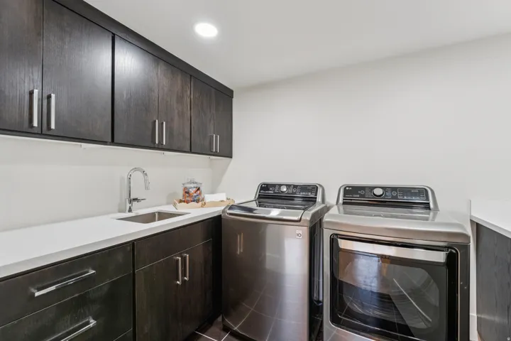 Laundry room featuring dark wood-finish cabinetry, white countertops, an undermount sink with a gooseneck faucet, and recessed lighting