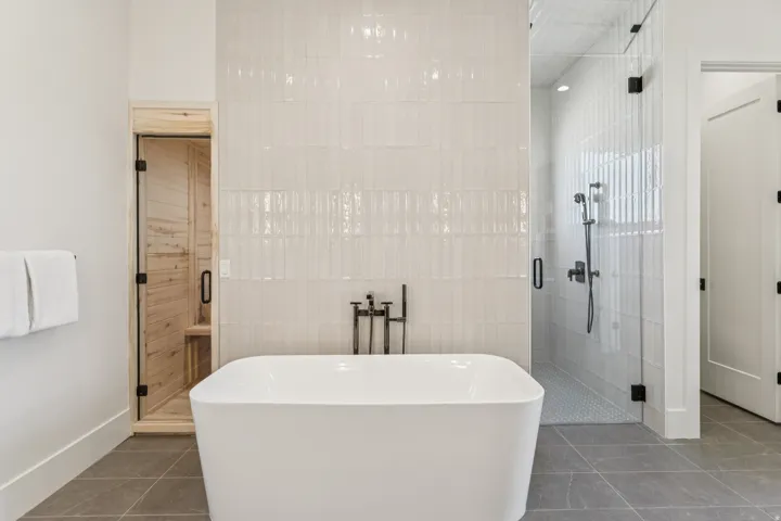 Freestanding soaking tub with floor-mounted fixtures, glass-enclosed shower with a rainfall showerhead, and a separate sauna with a glass door