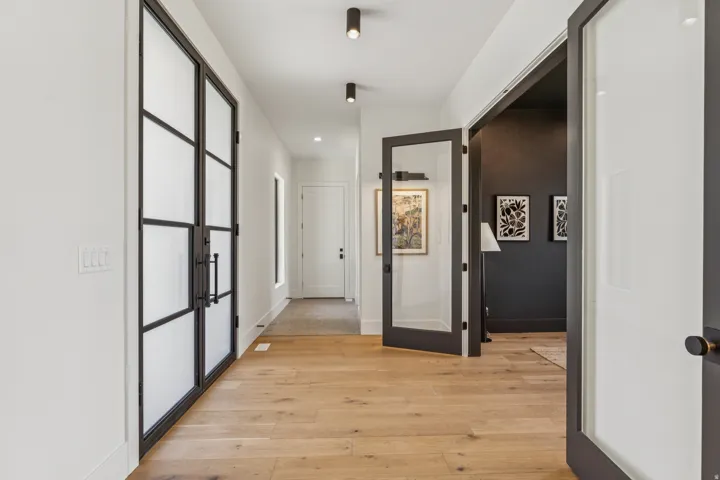 Wide plank wood-finish flooring extends through a bright hallway featuring white walls and recessed lighting