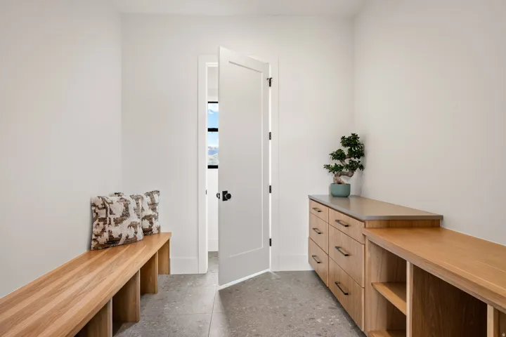Modern entryway featuring a light wood bench, built-in cabinetry with drawers and open shelving, gray speckled flooring, white walls, and a contemporary door with matte black hardware