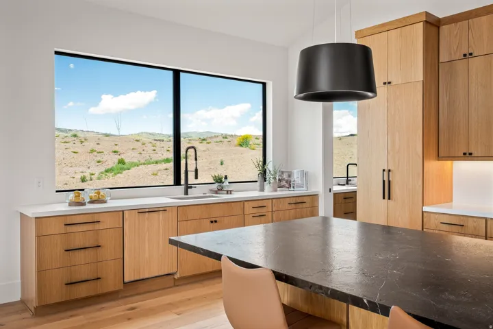 Expansive kitchen featuring a large window, light wood cabinetry, white countertops, a black island countertop, and wood-finish flooring