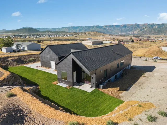 Modern architectural residence featuring a dark exterior, a prominent gable roofline, multiple windows, a concrete patio, and a newly installed lawn