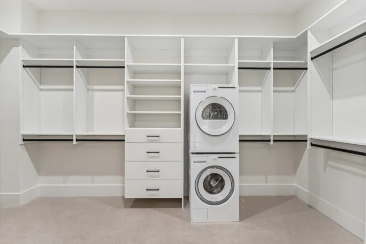 Custom closet system featuring extensive shelving, hanging rods, built-in drawers, and a stacked washer and dryer unit