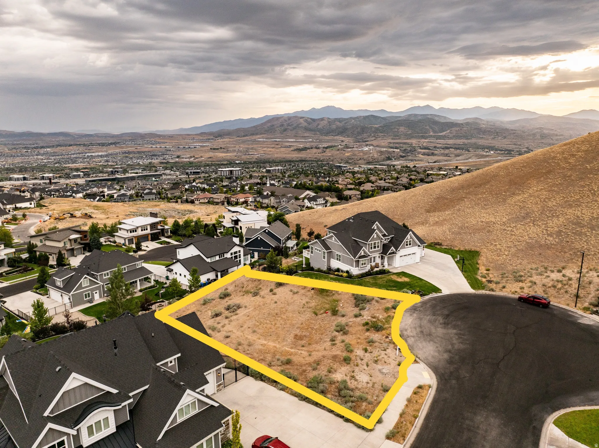 Expansive vacant lot featuring a paved street frontage, surrounding residential properties, and distant mountain scenery