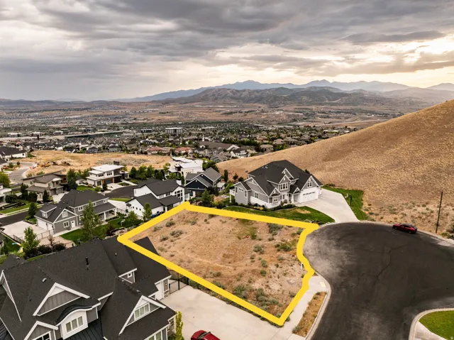 Expansive vacant lot featuring a paved street frontage, surrounding residential properties, and distant mountain scenery