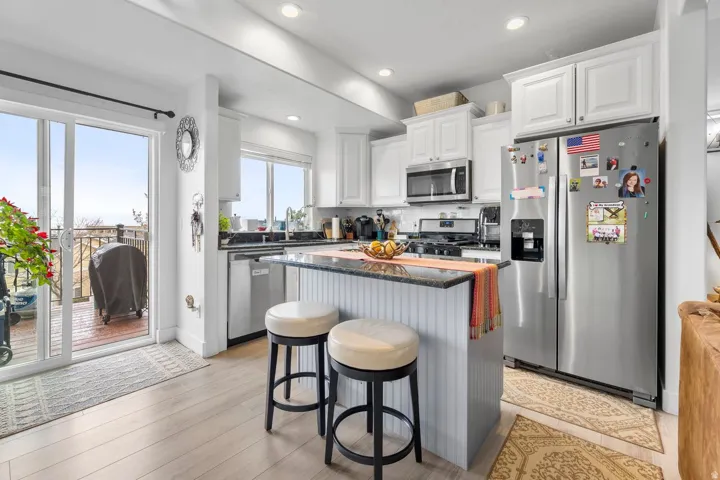 Kitchen featuring light wood-finish flooring, white cabinetry, stainless steel appliances, and a central island with a dark countertop