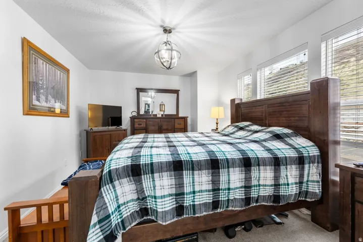 Spacious bedroom featuring light-colored walls, multiple windows with blinds, and a contemporary ceiling light fixture