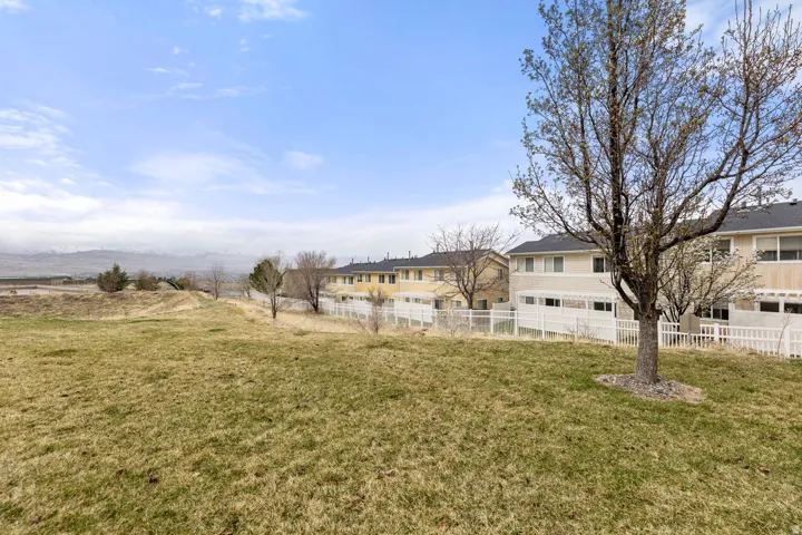 Expansive grassy area featuring a mature deciduous tree, a white picket fence, and distant mountain scenery