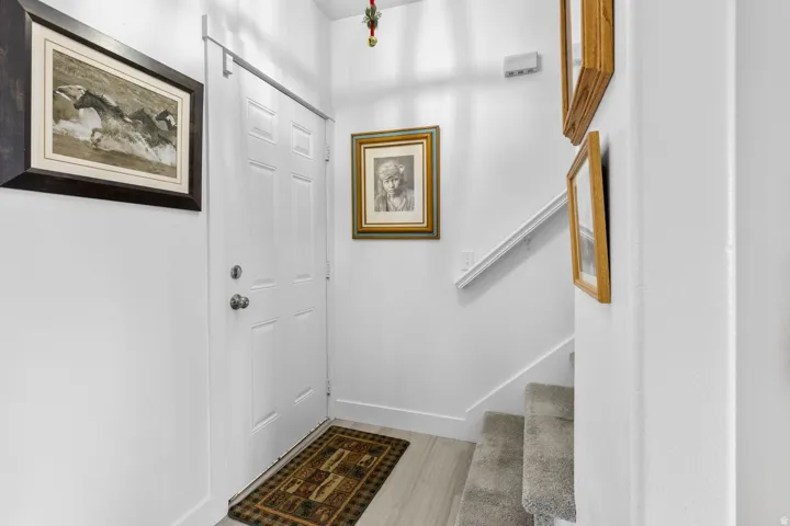 Entryway featuring a paneled door, wood-finish flooring, and a carpeted staircase with a white handrail