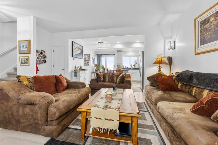 Open-concept living area featuring light wood-finish flooring, white walls, a staircase with carpeted treads, and recessed lighting