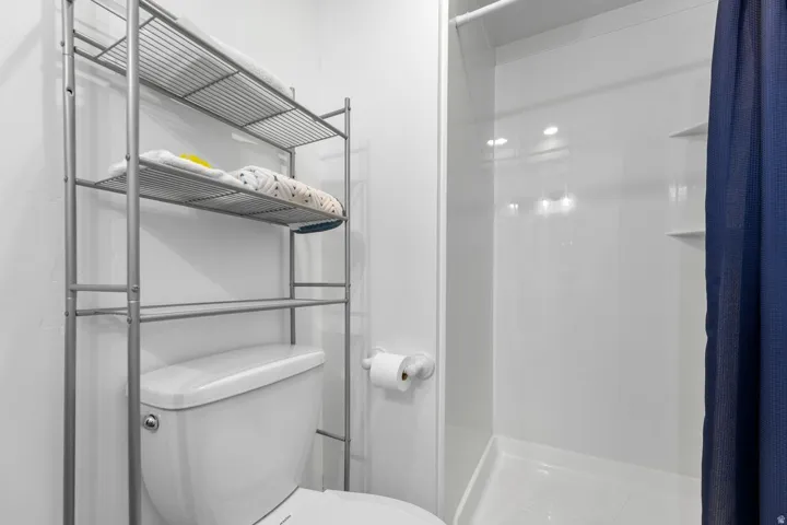 White-paneled shower with built-in shelving, complemented by a simple toilet and an over-toilet storage rack