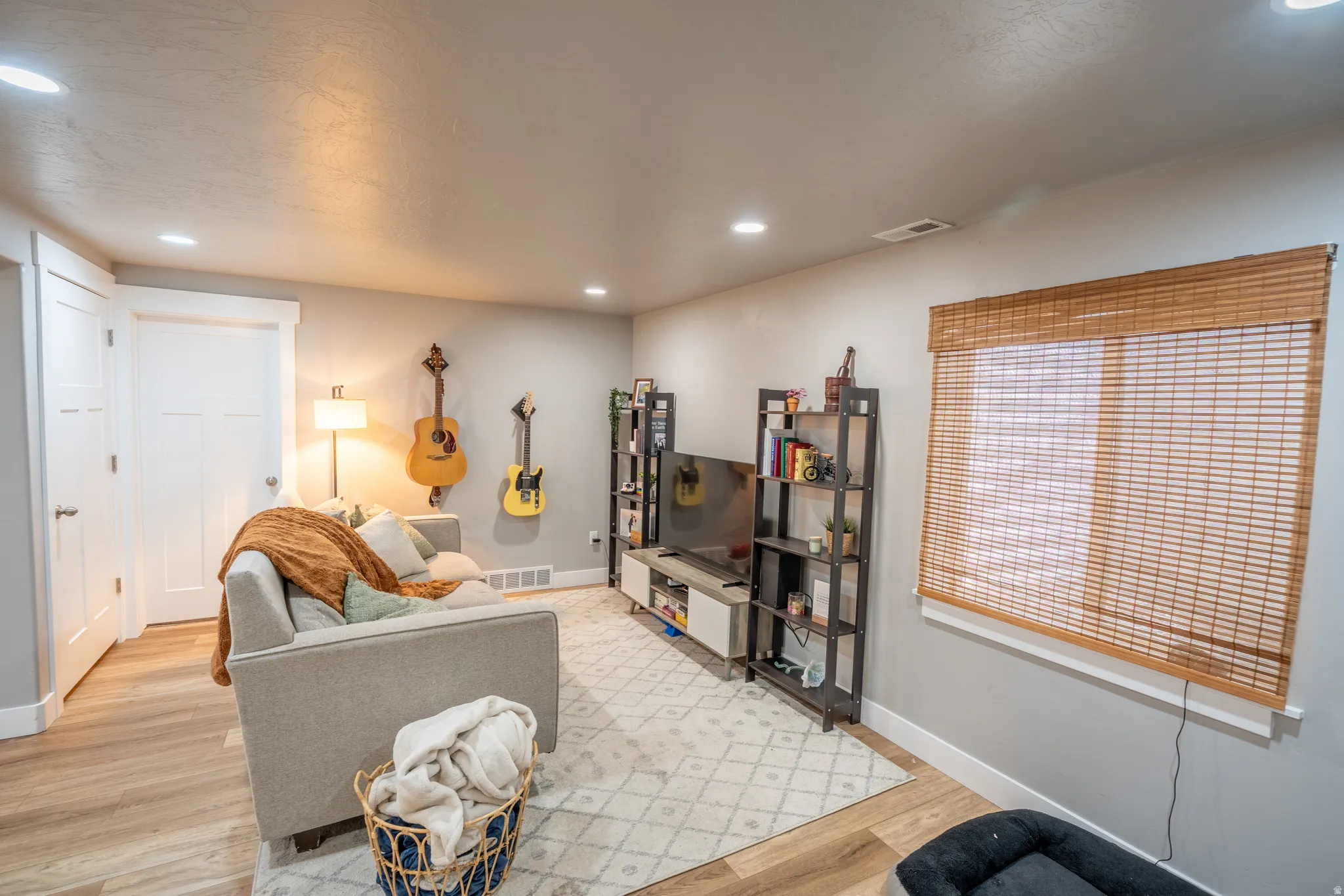 Spacious room featuring wood-finish flooring, recessed lighting, and a window with a woven wood shade