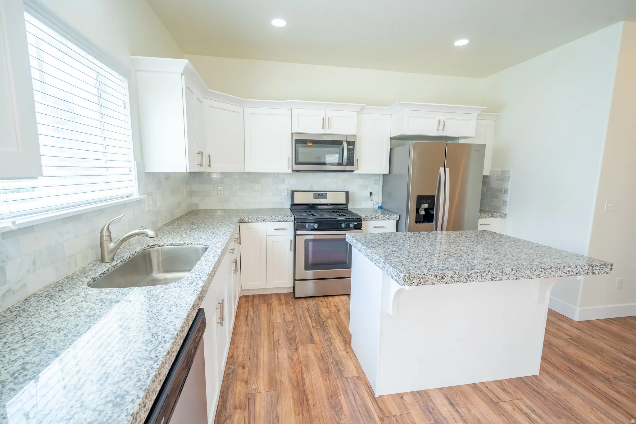 Kitchen featuring white cabinetry, stainless steel appliances, granite countertops, and wood-finish flooring