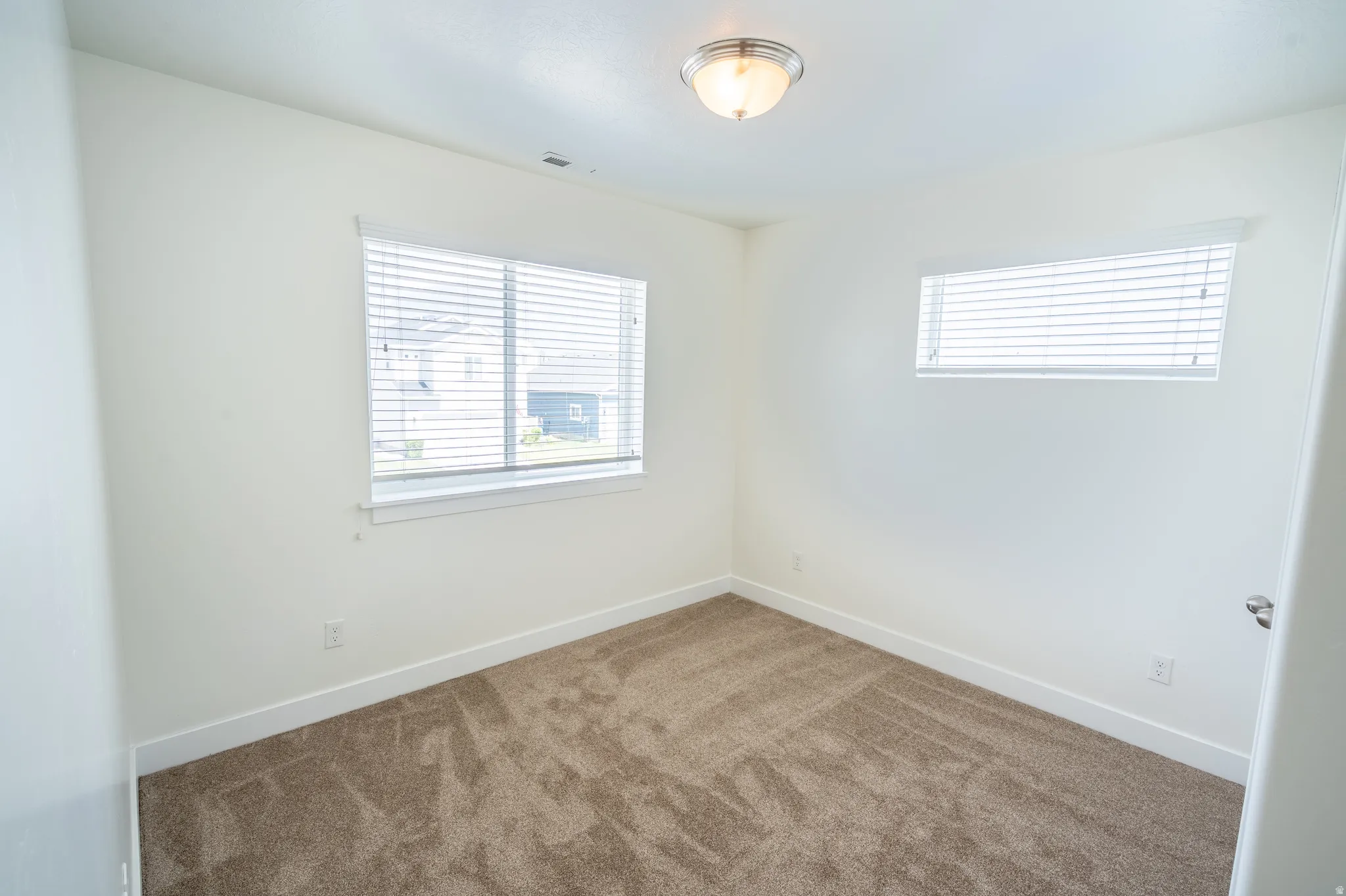 Neutral wall paint with white trim, a flush mount ceiling light fixture, and two windows with blinds