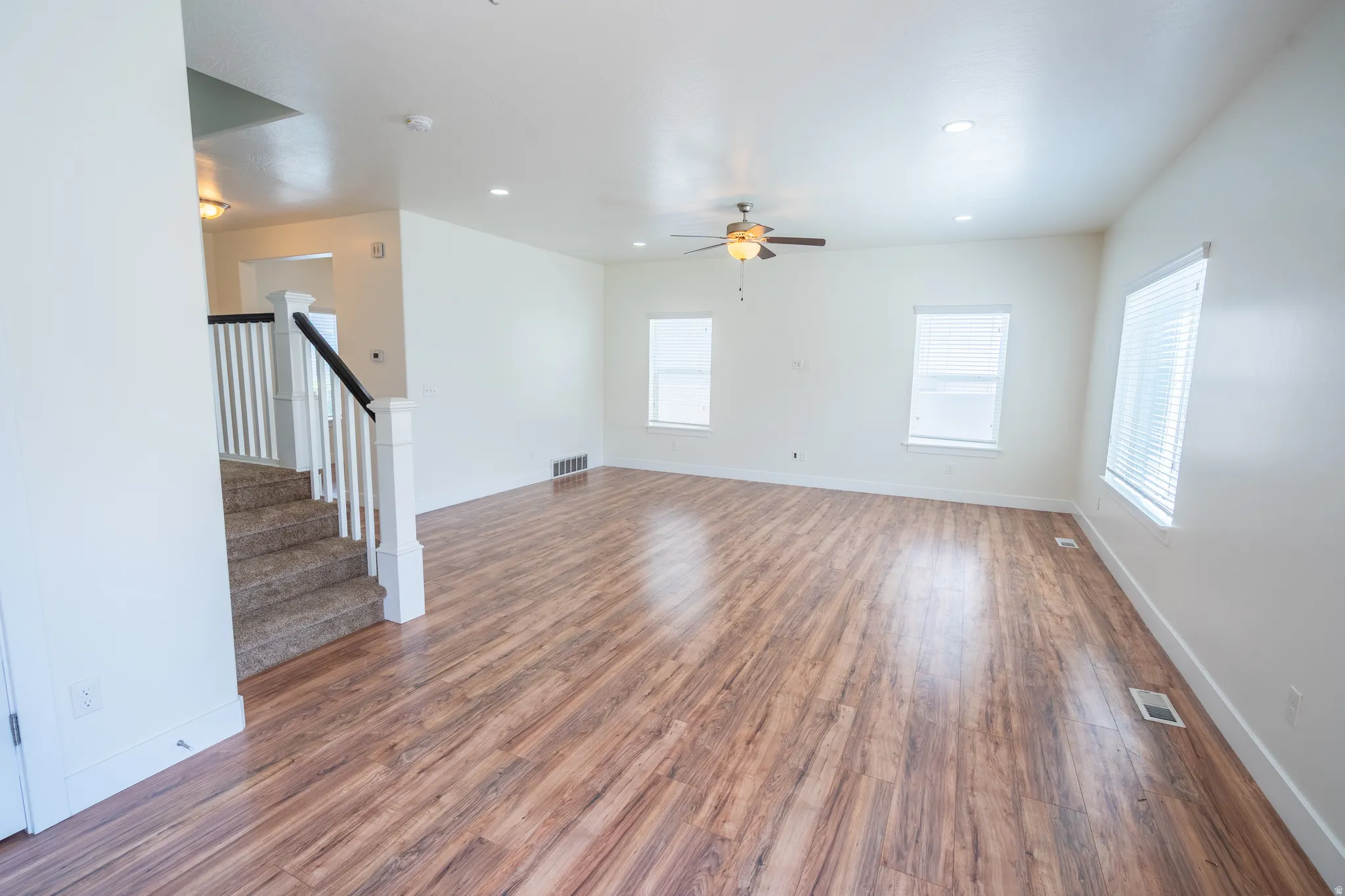 Spacious room featuring wood-finish flooring, white walls, and a ceiling fan with integrated lighting