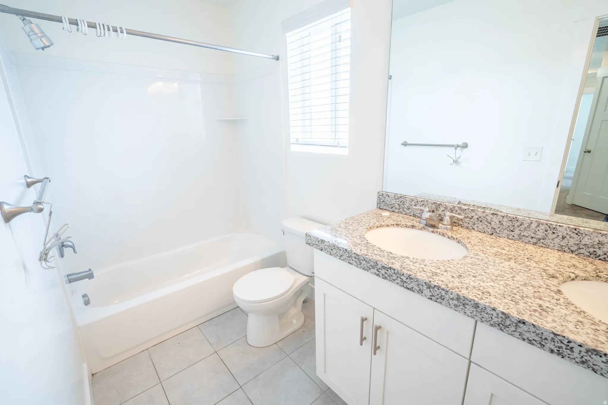Bathroom featuring a double vanity with stone countertops, integrated sinks, white cabinetry with brushed nickel hardware, and a tub/shower combination with a shower curtain rod