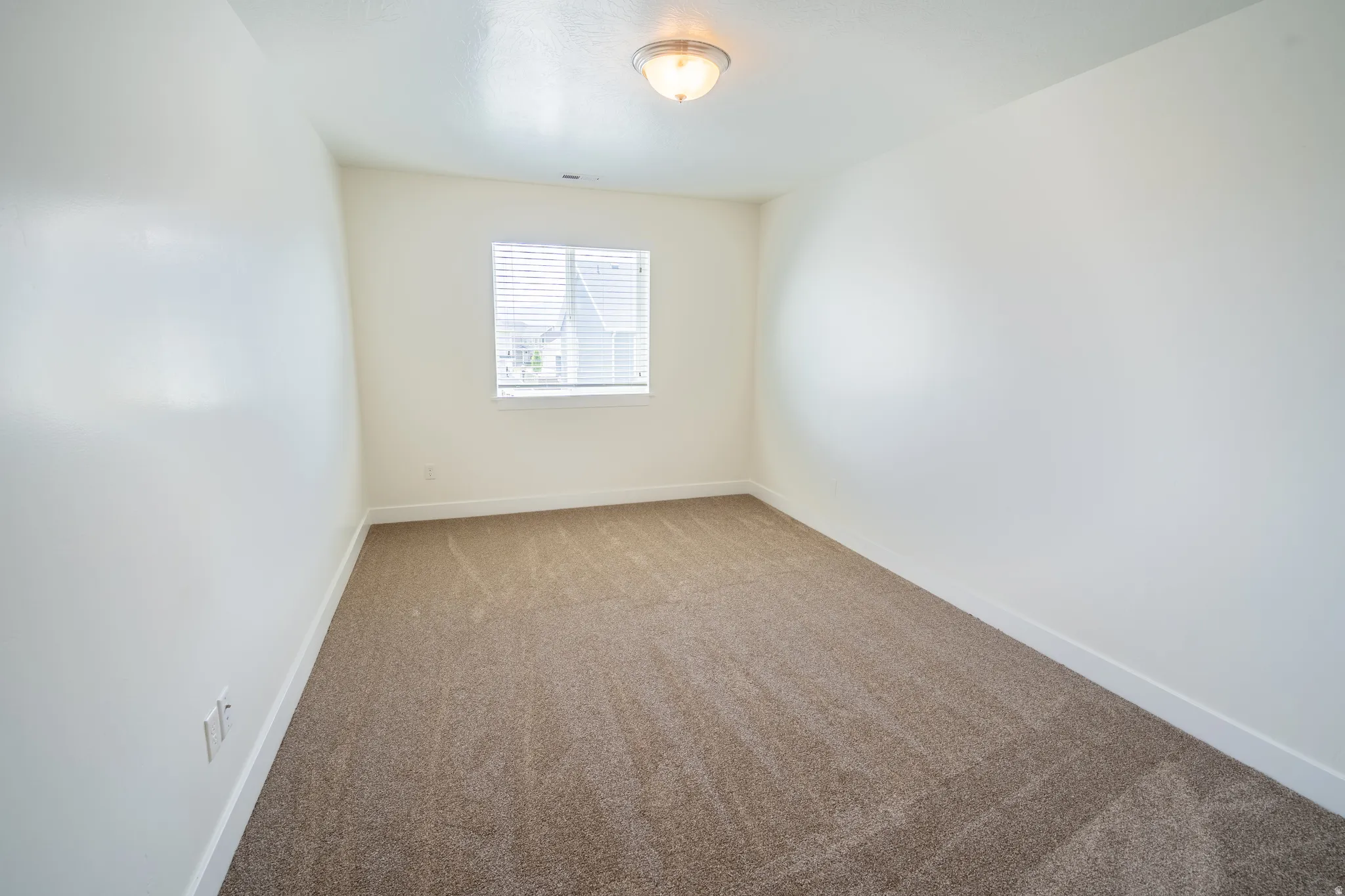 Carpeted room with white walls, a single window featuring horizontal blinds, and a flush-mount ceiling light fixture