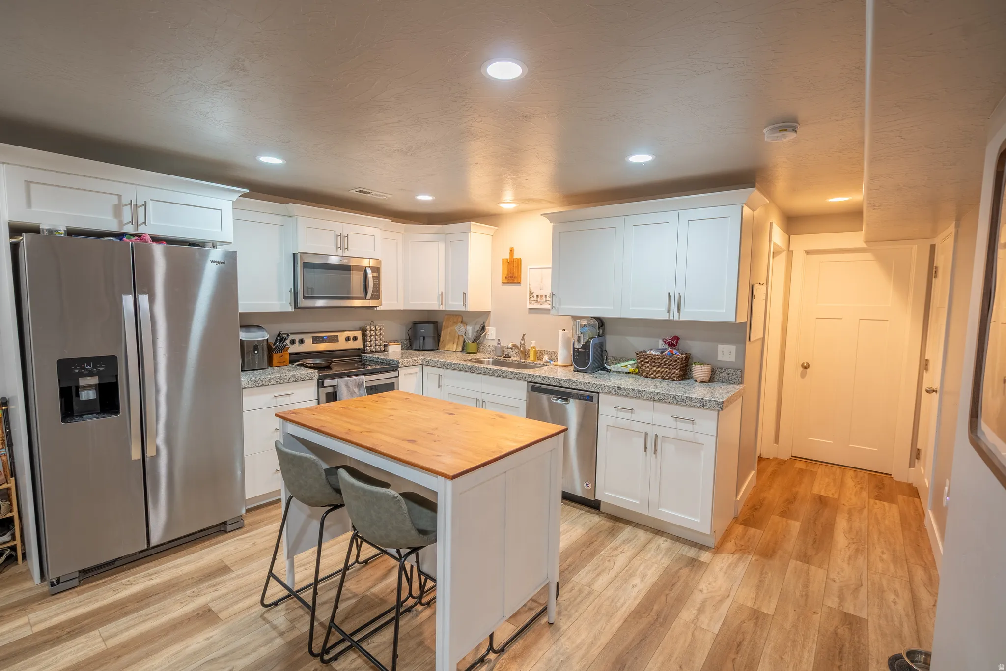 Kitchen featuring white cabinetry, stainless steel appliances, and wood-finish flooring
