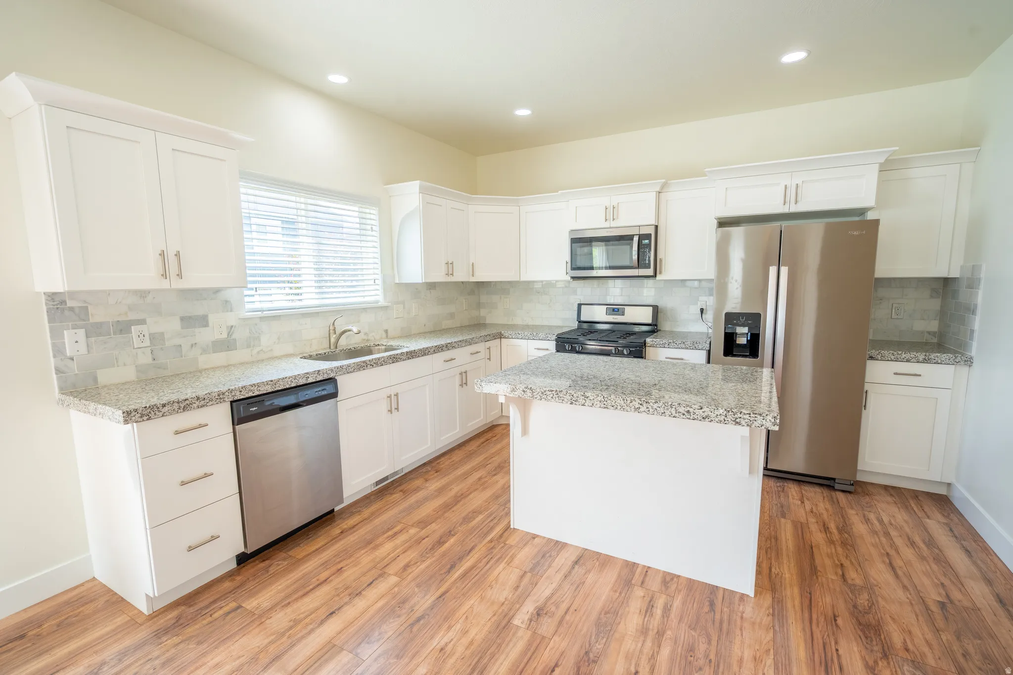 Kitchen featuring white cabinetry, wood-finish flooring, stainless steel appliances, speckled countertops, and a full tile backsplash