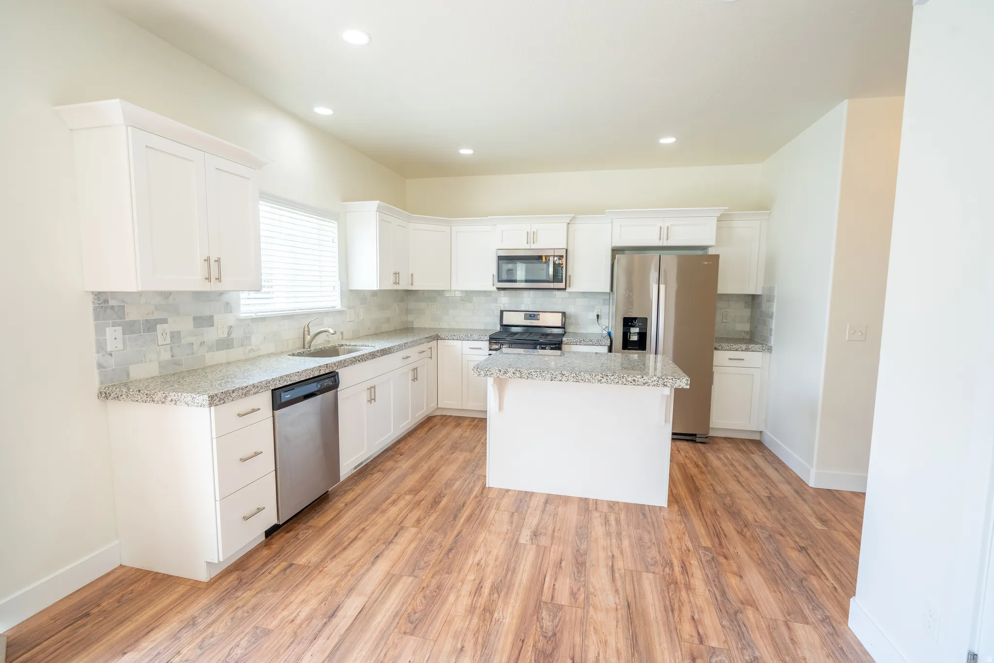 Kitchen featuring white shaker cabinetry, stainless steel appliances, speckled stone countertops, and a stone tile backsplash