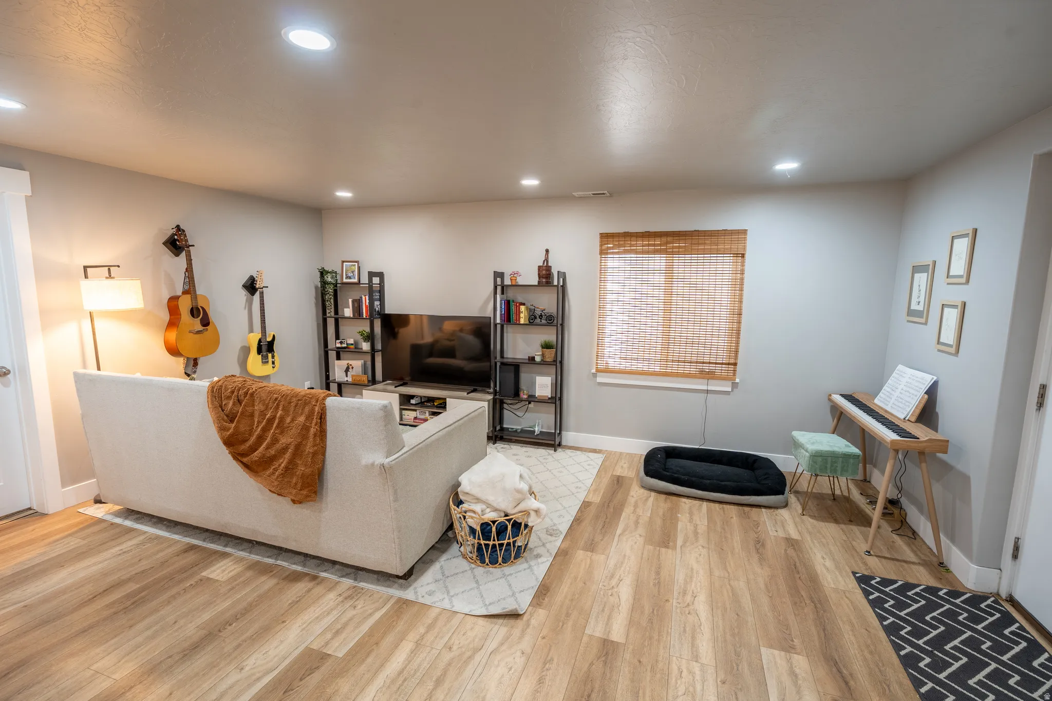 Spacious room featuring light wood-finish flooring, recessed lighting, and a window with natural woven blinds