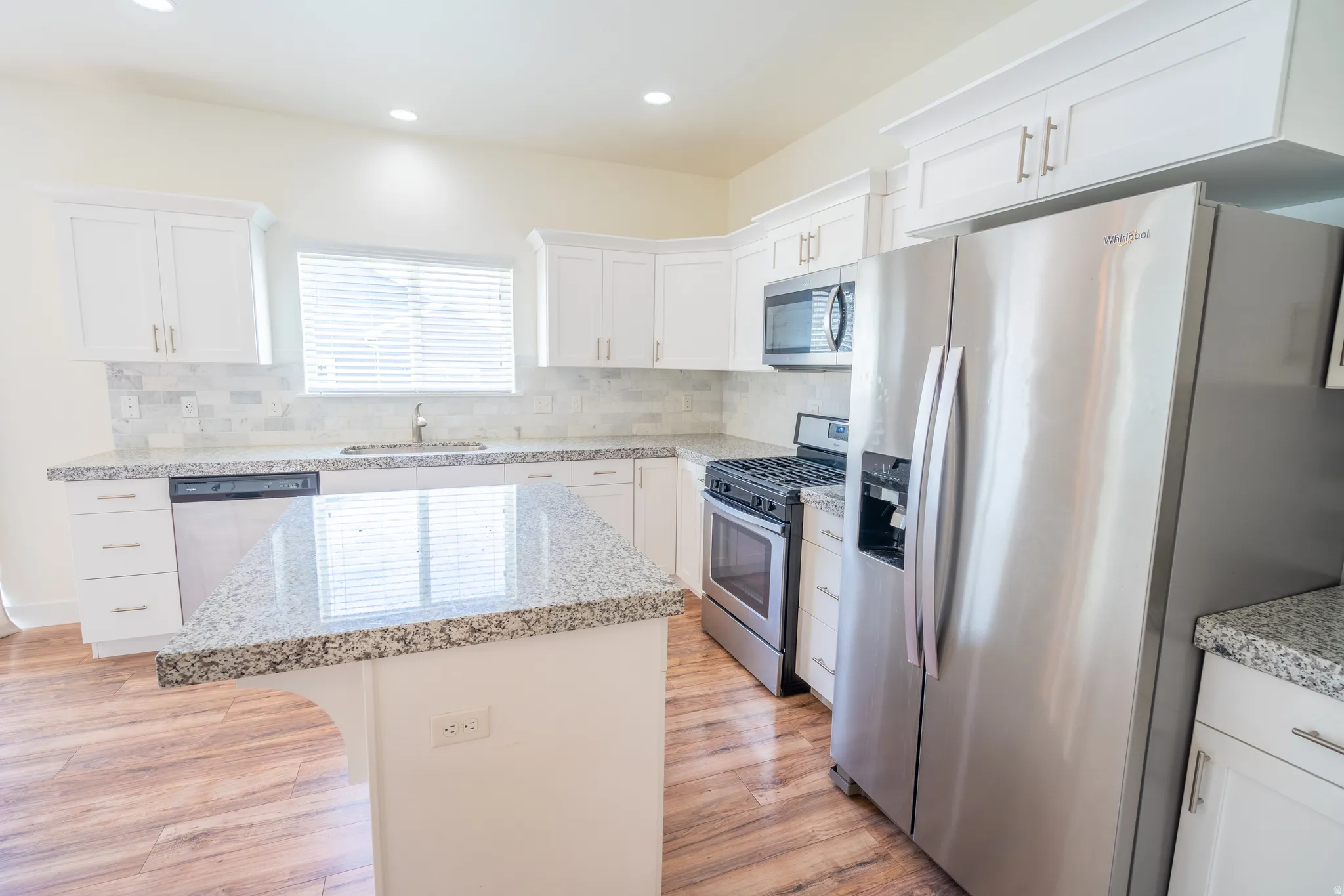 Kitchen featuring white shaker cabinetry, stainless steel appliances, speckled stone countertops, a tile backsplash, and wood-finish flooring