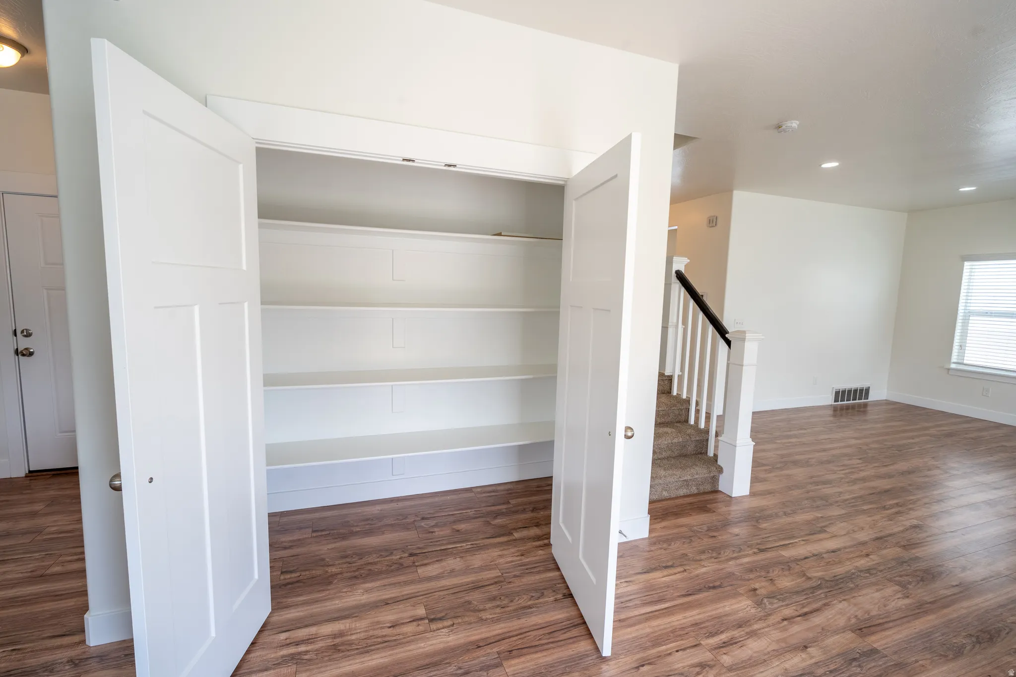 Built-in white shelving, wood-finish flooring, white paneled doors, white walls, and a staircase with white balusters and a dark handrail