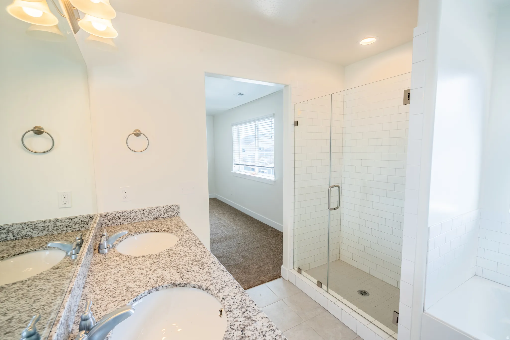 Bathroom featuring a double vanity with stone-finish countertops, dual undermount sinks, and a framed glass shower enclosure with subway tile surround