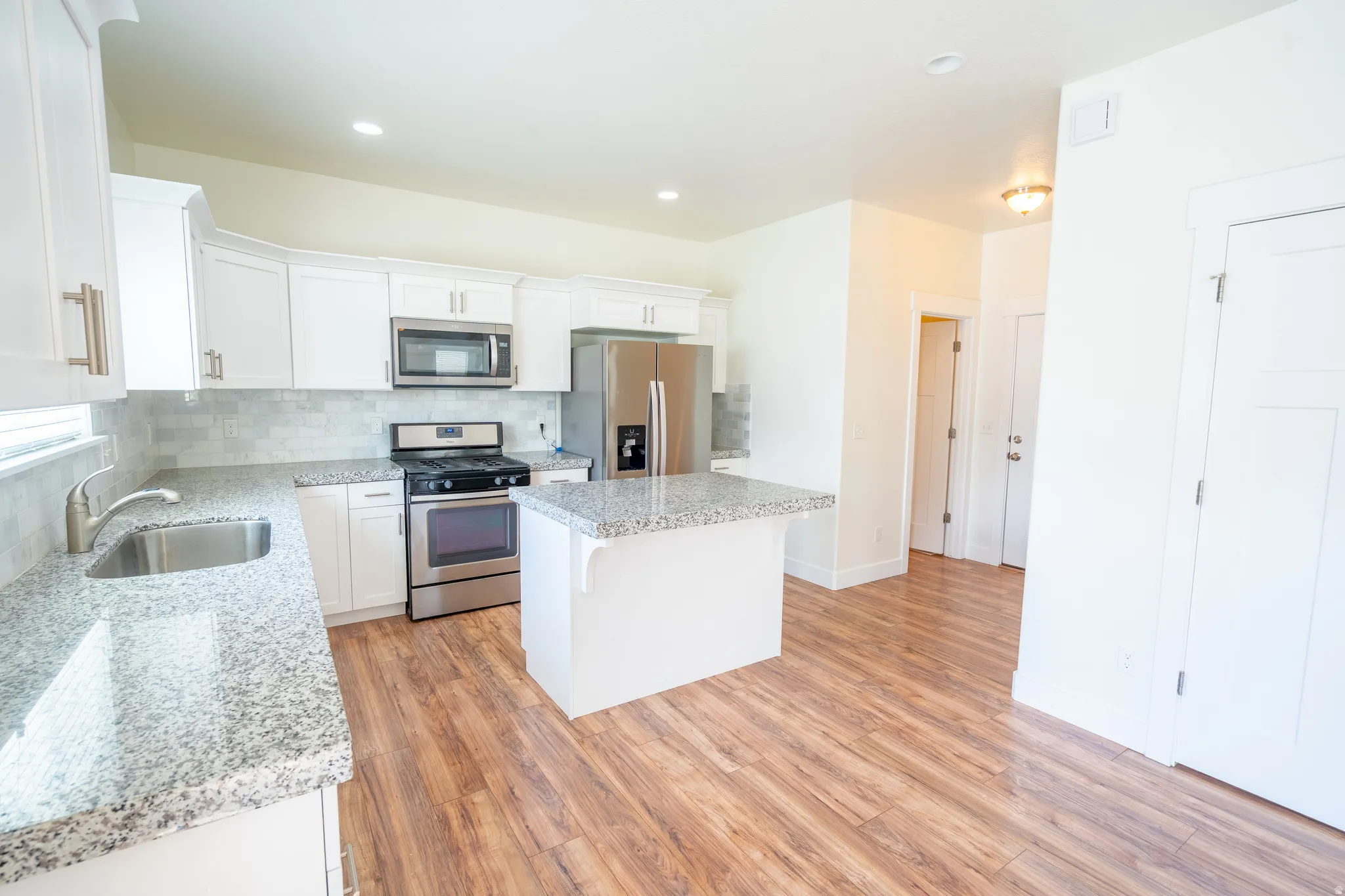 Kitchen featuring white cabinetry, stainless steel appliances, speckled stone countertops, a tile backsplash, and wood-finish flooring