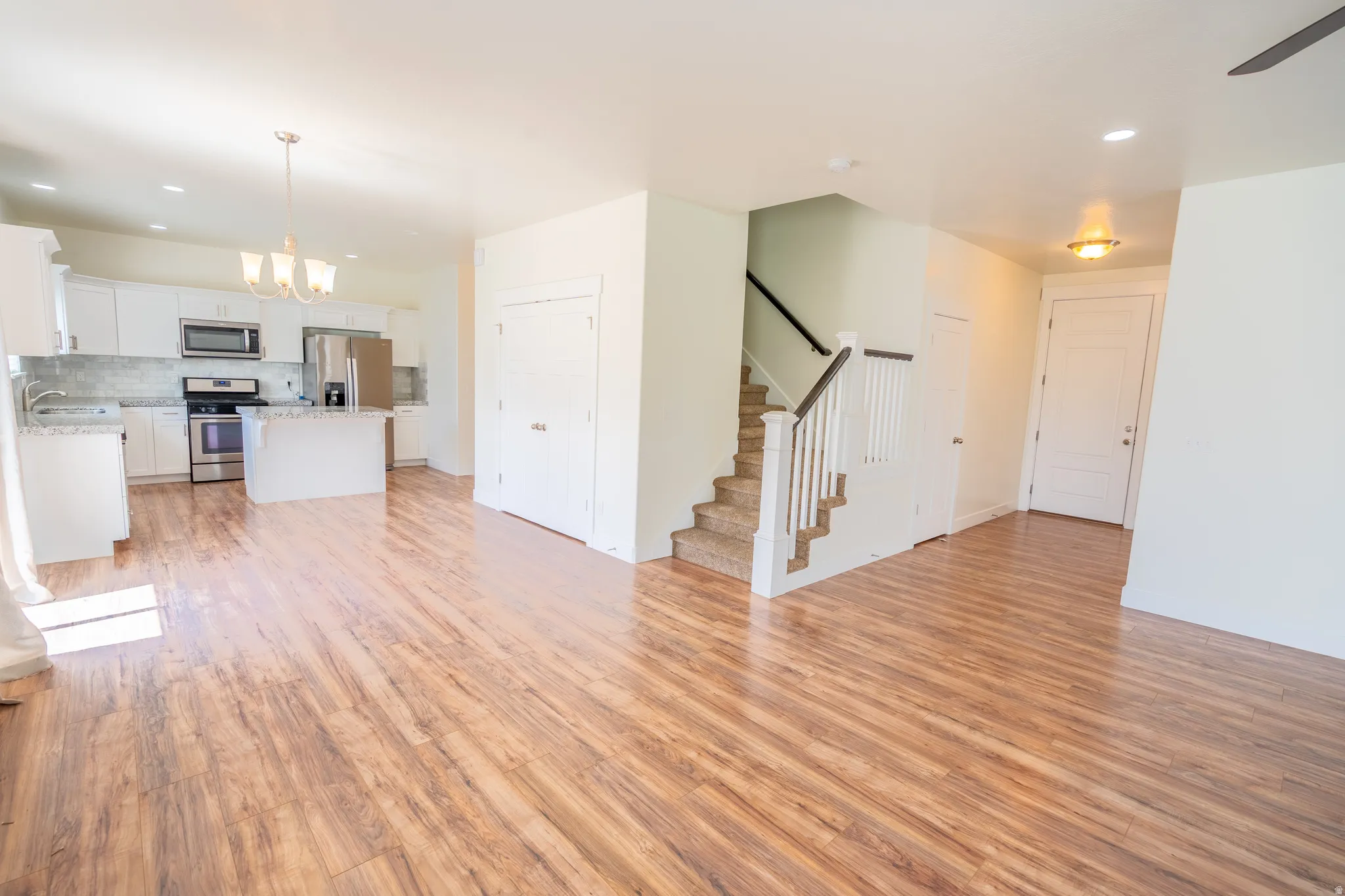 Open-concept living space featuring wood-finish flooring, a contemporary kitchen with white cabinetry, a kitchen island, and stainless steel appliances