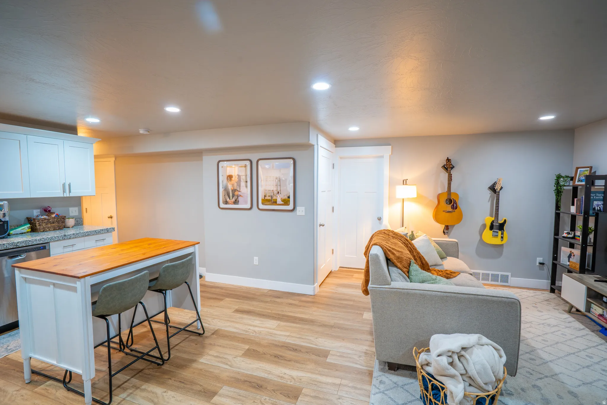 Open-concept living space featuring wood-finish flooring, recessed lighting, a kitchen island with seating, white shaker cabinetry, and granite-style countertops