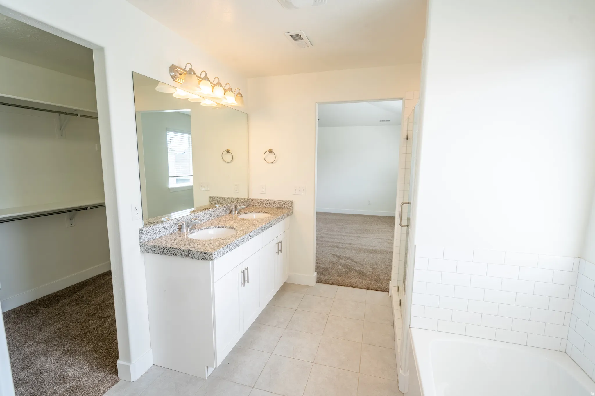 Bathroom featuring a dual-sink vanity with a granite-style countertop, white cabinetry, and a large mirror