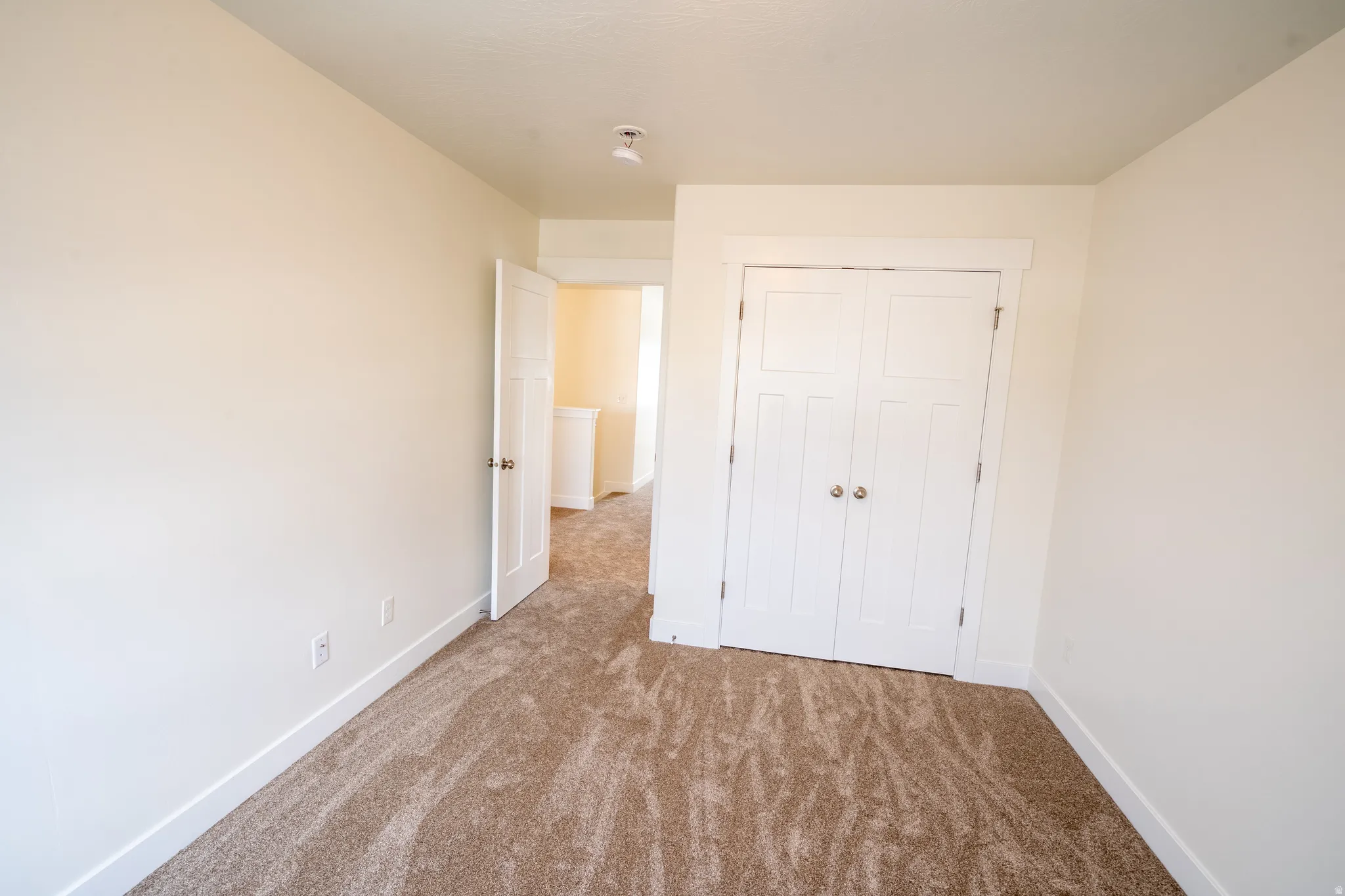 Neutral-toned room featuring plush carpeting, white baseboards, and a double-door closet with gold-toned hardware