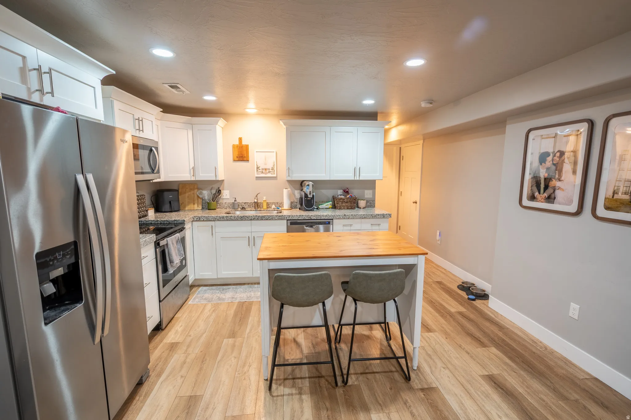 Kitchen featuring white shaker cabinetry, stainless steel appliances, light-toned wood-finish flooring, a central island with a wood countertop, and recessed lighting
