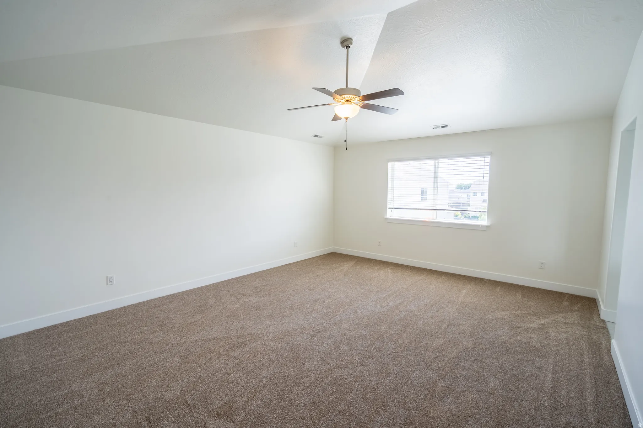 Spacious room featuring neutral carpeting, white walls, and a ceiling fan with light fixture