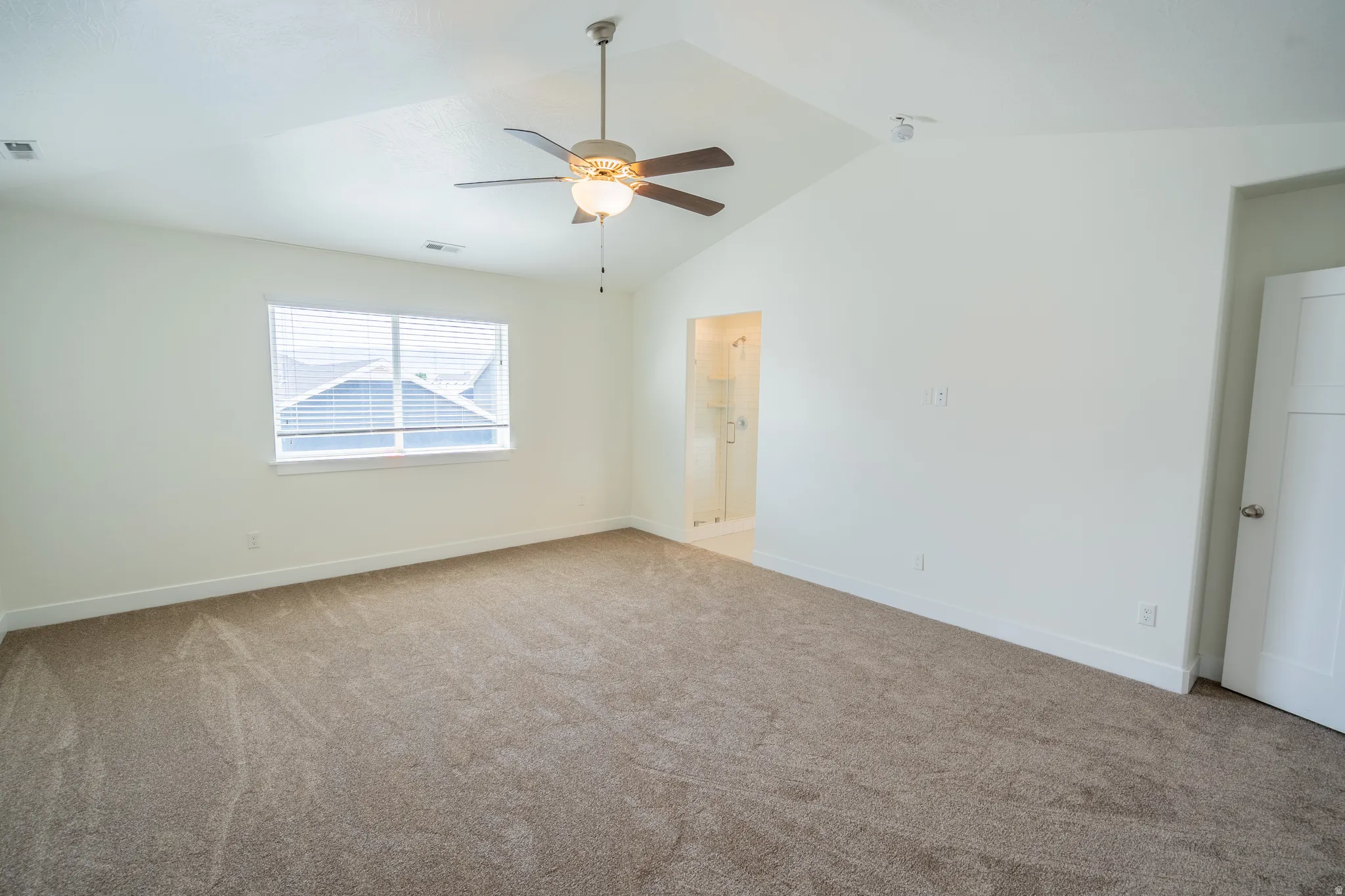Spacious room featuring vaulted ceilings, a ceiling fan with integrated lighting, and neutral-toned carpet flooring