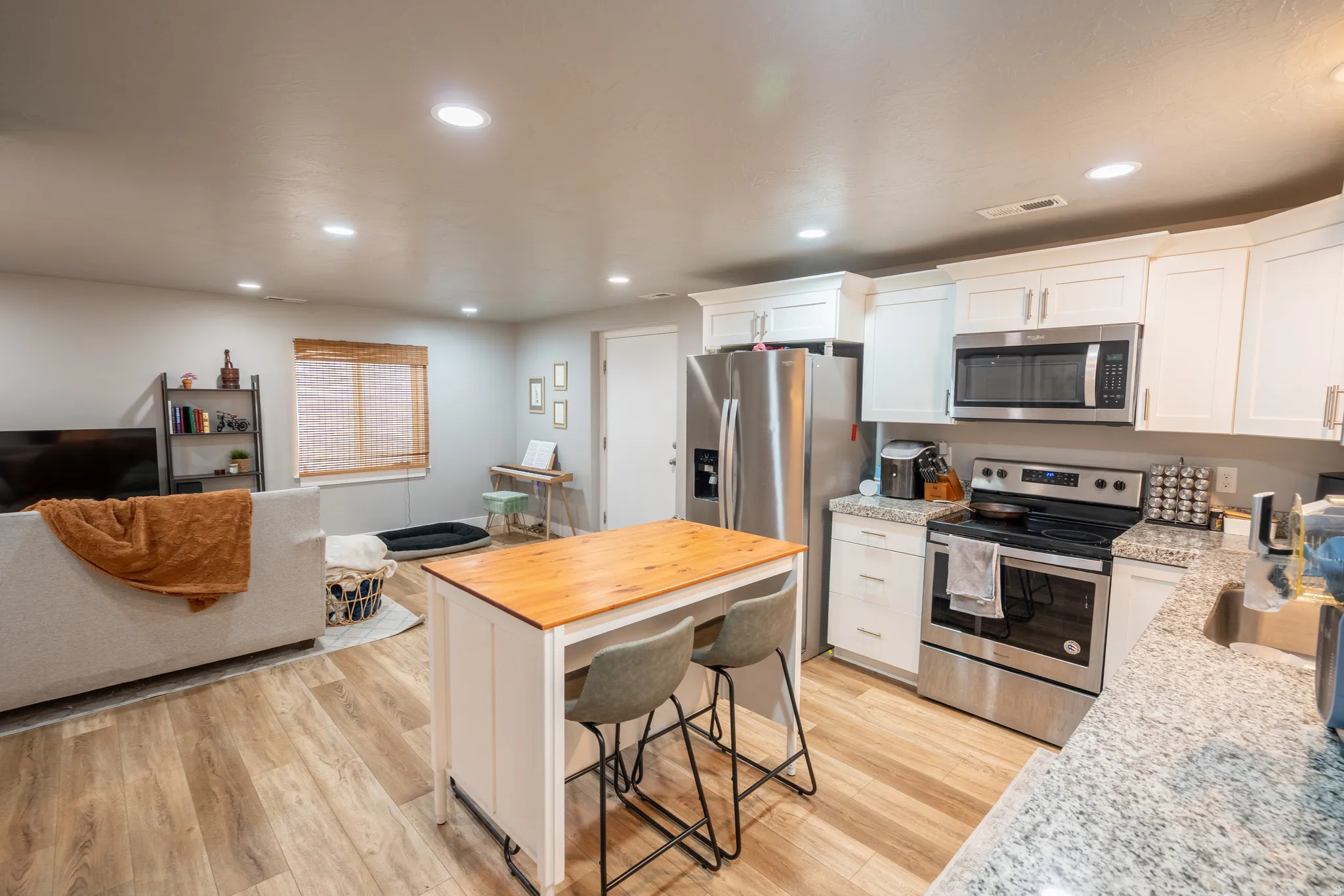 Open-concept living space featuring wood-finish flooring, recessed lighting, and a kitchen with white cabinetry, stainless steel appliances, and stone countertops