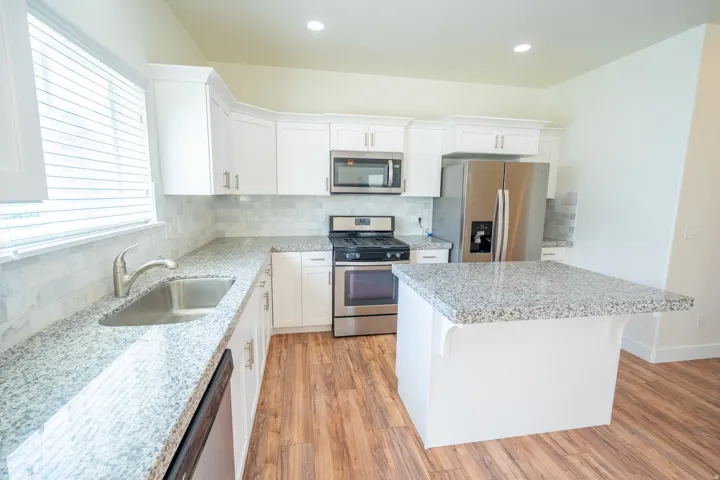 Kitchen featuring white cabinetry, stainless steel appliances, granite countertops, and wood-finish flooring