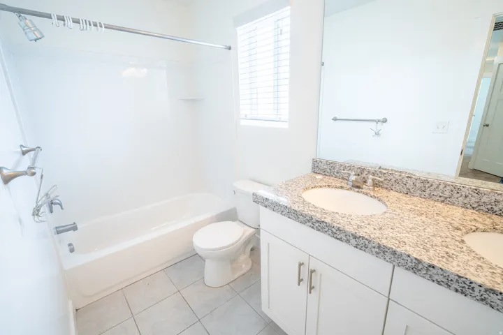 Bathroom featuring a double vanity with stone countertops, integrated sinks, white cabinetry with brushed nickel hardware, and a tub/shower combination with a shower curtain rod